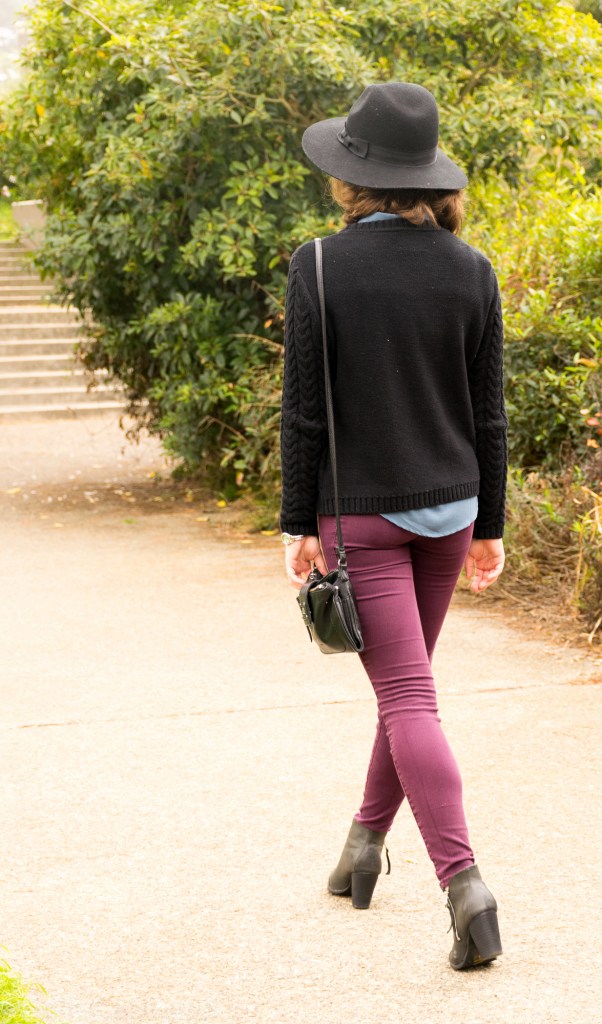 Black hat, black sweater with blue collar, eggplant pants, black booties, long bob, cross body purse